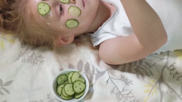 Pequeña hermosa chica hermosa está haciendo máscaras de pepino en casa y comer verduras — Vídeos de Stock