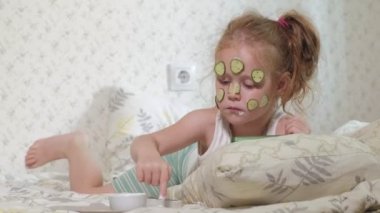 Küçük bir güzel kız neşeyle bir salatalık maskesi evde yapar ve bir akıllı telefon kullanır