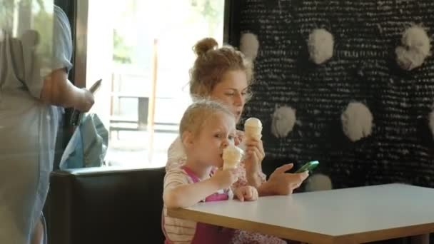 Een jonge moeder en haar dochtertje doorbrengen tijd in een restaurant in een traag tempo. Eten van ijs — Stockvideo