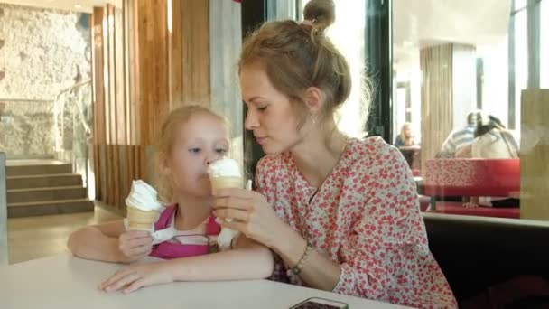 Una madre joven y su hija pequeña pasan tiempo en un restaurante a un ritmo lento. Comer helado — Vídeos de Stock