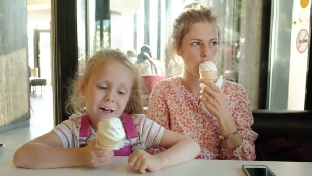 Una madre joven y su hija pequeña pasan tiempo en un restaurante a un ritmo lento. Comer helado — Vídeo de stock