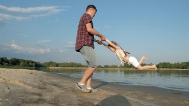 Närbild av far och dotter leker tillsammans. En ung fader snurrar sin dotter vid stranden av havet stranden super slow motion — Stockvideo