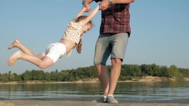 Närbild av far och dotter leker tillsammans. En ung fader snurrar sin dotter vid stranden av havet stranden super slow motion — Stockvideo