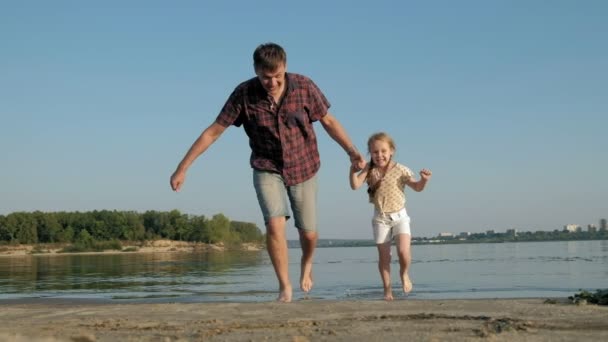 Närbild av far och dotter leker tillsammans. En ung fader snurrar sin dotter vid stranden av havet stranden super slow motion — Stockvideo