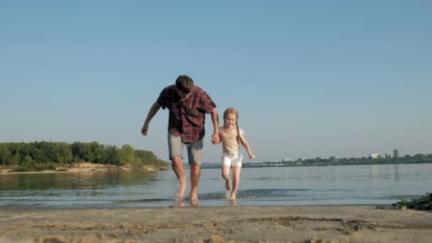 Zbliżenie: ojciec i córka grać razem. Młody ojciec jest spinning jego córka na plaży Morza brzeg super zwolnionym tempie — Wideo stockowe