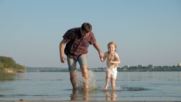 Close-up de pai e filha brincando juntos. Um jovem pai está girando sua filha na praia da costa do mar super câmera lenta — Vídeo de Stock