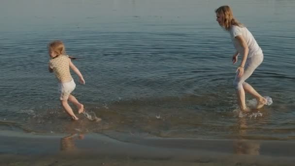 Close-up van moeder en dochter samen spelen. Een jonge moeder draait zijn dochter op het strand van de zee oever super slow motion — Stockvideo