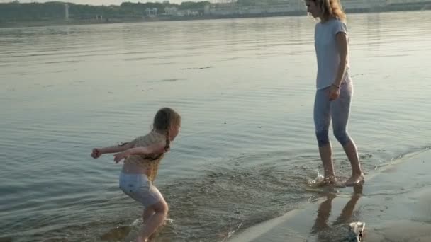 Close-up de mãe e filha brincando juntos. Uma jovem mãe está girando sua filha na praia da costa do mar super câmera lenta — Vídeo de Stock