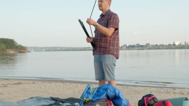 En mogen man samlar ett tält på semester utomhus nära havet — Stockvideo