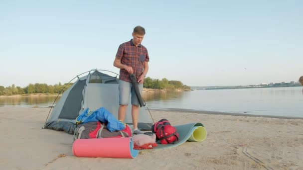 Ein reifer Mann sammelt im Urlaub draußen am Meer ein Zelt — Stockvideo