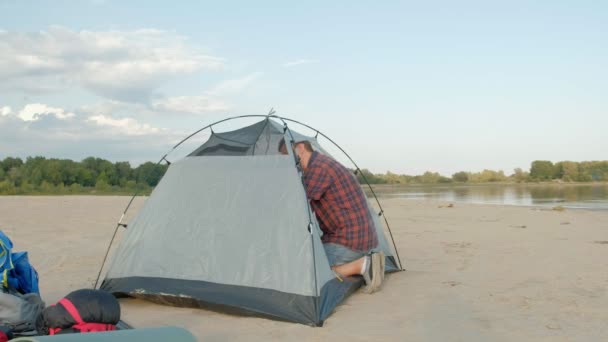 En mogen man samlar ett tält på semester utomhus nära havet — Stockvideo