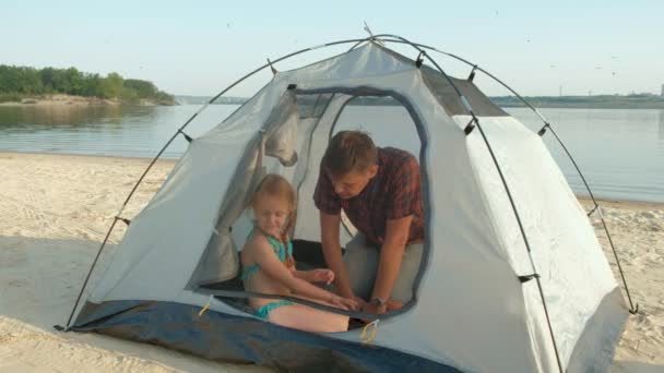Um homem maduro recolhe uma tenda em férias ao ar livre perto do mar — Vídeo de Stock