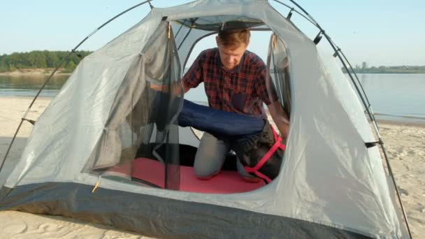 Взрослый мужчина собирает палатку на отдыхе на открытом воздухе у моря — стоковое видео