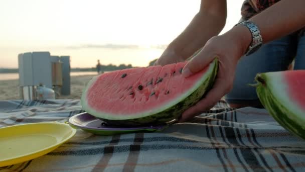 Happy girl eating slices of watermelon on the beach. Father slicing a watermelon Summer picnic outdoors. — Stock Video