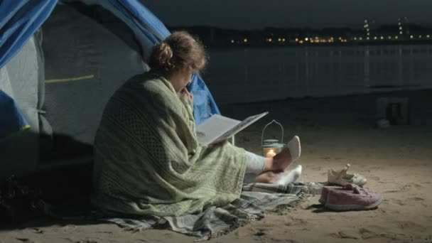 Mor och hennes vackra dotter läsa en bok nära turist tält på natten på stranden — Stockvideo