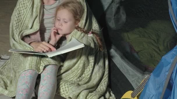 Мать и ее прекрасная дочь читали книгу возле туристической палатки ночью на пляже — стоковое видео