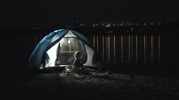 Мать и ее прекрасная дочь читали книгу возле туристической палатки ночью на пляже — стоковое видео
