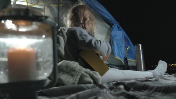 Uma menina bonita joga em um ukulele na margem do rio perto de uma tenda turística — Vídeo de Stock