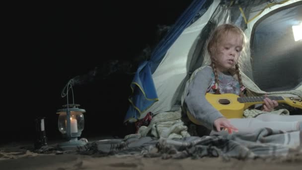 Une belle fille joue sur un ukulélé sur la rive d'une rivière près d'une tente touristique — Video