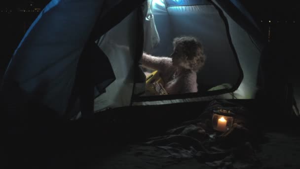 Een mooi meisje en vrouw speelt op een ukulele aan de rivieroever in de buurt van een toeristische tent — Stockvideo