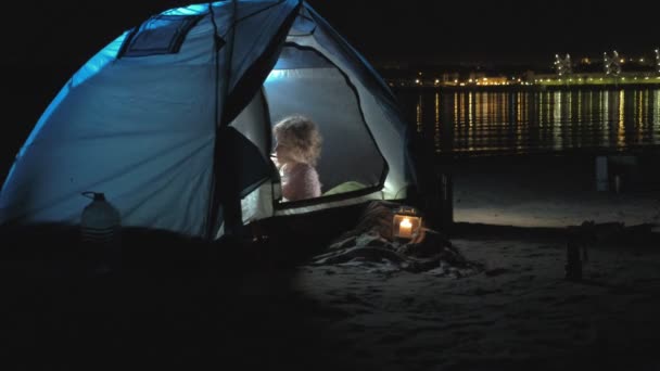 Una bella ragazza e donna gioca su un ukulele sulla riva del fiume vicino a una tenda turistica — Video Stock