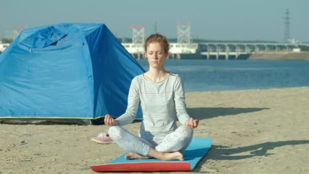 Belle femme faisant du yoga en mer, harmonie et liberté, arrière-plan de la mer et sable tente touristique bleue, concept de yoga et de paix pendant les vacances — Video