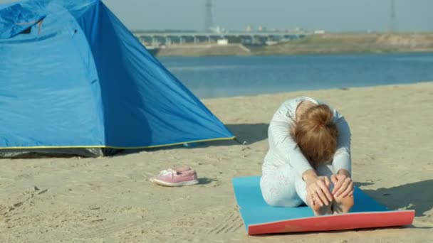 Schöne Frau, die Yoga auf See macht, Harmonie und Freiheit, Hintergrund vom Meer und sandblaues Touristenzelt, Konzept von Yoga und Frieden im Urlaub — Stockvideo