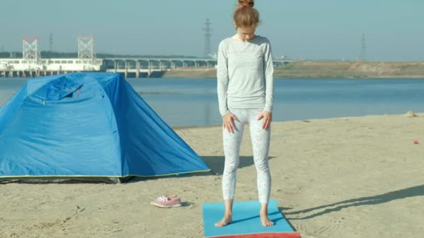 Belle femme faisant du yoga en mer, harmonie et liberté, arrière-plan de la mer et sable tente touristique bleue, concept de yoga et de paix pendant les vacances — Video