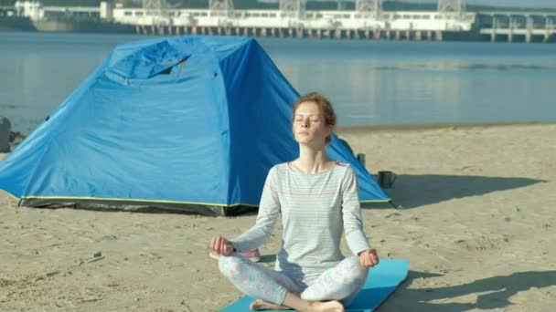 Mooie vrouw doen yoga op zee, harmonie, concept van yoga en vrede en vrijheid, achtergrond van zee en zand blauw toeristische tent tijdens vakantie — Stockvideo