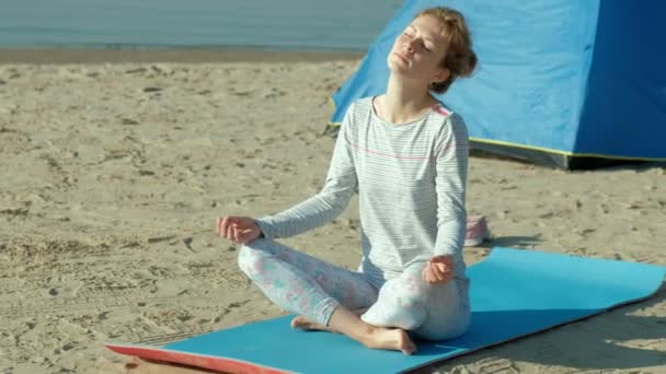 Bella donna che fa yoga in mare, armonia e libertà, sfondo da mare e sabbia tenda turistica blu, concetto di yoga e pace durante le vacanze — Video Stock