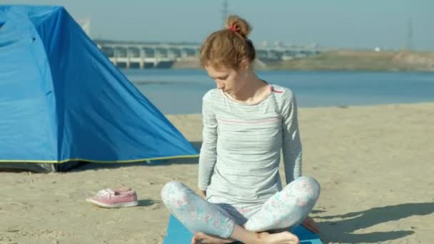Beautiful woman doing yoga at sea, harmony and freedom, background from sea and sand blue tourist tent, concept of yoga and peace during holidays — Stock Video