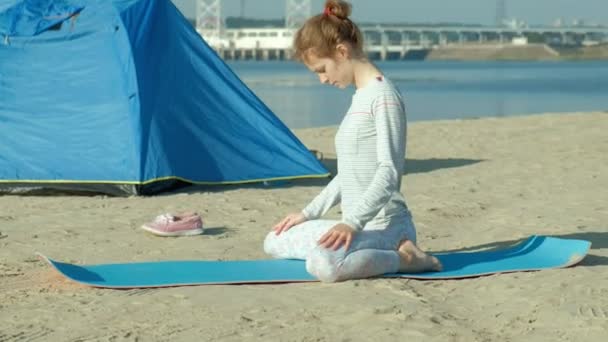 Belle femme faisant du yoga en mer, harmonie et liberté, arrière-plan de la mer et sable tente touristique bleue, concept de yoga et de paix pendant les vacances — Video