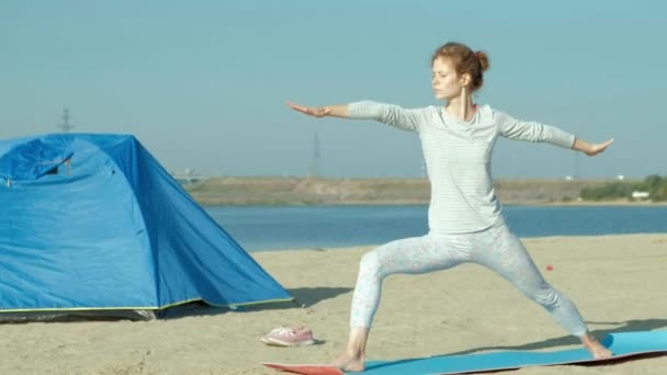 Schöne Frau, die Yoga auf See macht, Harmonie und Freiheit, Hintergrund vom Meer und sandblaues Touristenzelt, Konzept von Yoga und Frieden im Urlaub — Stockvideo