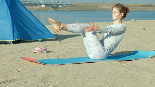 Schöne Frau, die Yoga auf See macht, Harmonie und Freiheit, Hintergrund vom Meer und sandblaues Touristenzelt, Konzept von Yoga und Frieden im Urlaub — Stockvideo