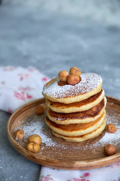 Pancakes sprinkled with nuts hazelnuts on a plate with a napkin on a concrete background — Stock Photo, Image