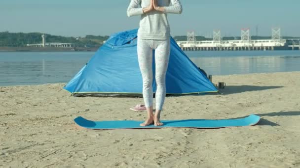 Vacker kvinna gör yoga vid havet, harmoni och frihet, bakgrund från hav och sand blå turist tält, begreppet yoga och fred under helgdagar — Stockvideo