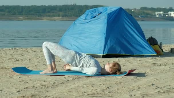 Schöne Frau, die Yoga auf See macht, Harmonie und Freiheit, Hintergrund vom Meer und sandblaues Touristenzelt, Konzept von Yoga und Frieden im Urlaub — Stockvideo