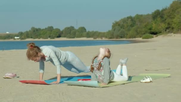 Mor och dotter är engagerade i yoga till sjöss, ler, bakgrund av blå havsvatten. begreppet familj, mor och dotter vänskap, semester. — Stockvideo