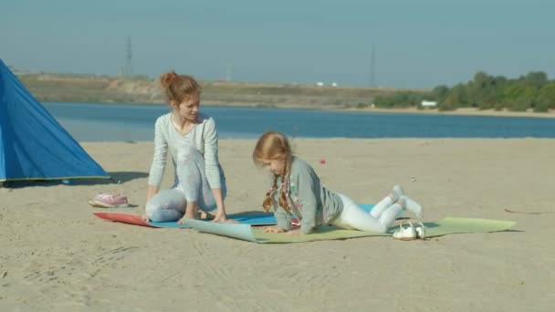 Moeder en dochter zijn verwikkeld in yoga op zee, zijn de glimlachen, de achtergrond van blauwe zeewater. concept van moeder en dochter vriendschap, familie, vakantie. — Stockvideo