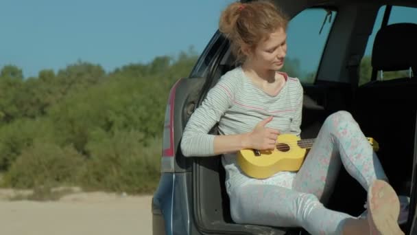 Kvinna som spelar på en ukulele i en öppen bål bil nära havet — Stockvideo