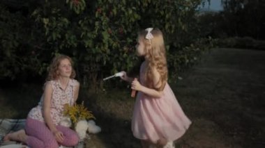 Mutlu anne ve kızı sabun köpüğü şişirmek. Aile içinde sıcak bir akşam günbatımında pikniğe üzerinde bir şehir parkı.