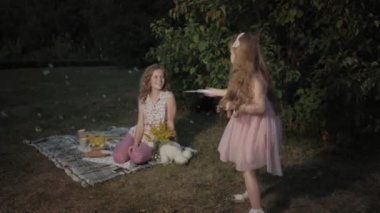 Mutlu anne ve kızı sabun köpüğü şişirmek. Aile içinde sıcak bir akşam günbatımında pikniğe üzerinde bir şehir parkı.