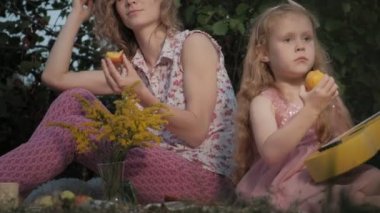 Mutlu anne ve kızı ukulele üzerinde oynuyorlar. Aile içinde sıcak bir akşam günbatımında pikniğe üzerinde bir şehir parkı.