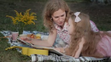 Mutlu anne ve kızı bir kitap okumak bir albümdeki fotoğrafları. Aile içinde sıcak bir akşam günbatımında pikniğe üzerinde bir şehir parkı.