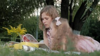 Mutlu anne ve kızı bir kitap okumak bir albümdeki fotoğrafları. Aile içinde sıcak bir akşam günbatımında pikniğe üzerinde bir şehir parkı.