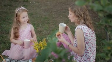 Mutlu anne ve kızı peçe üzerinde çay içiyor. Aile içinde sıcak bir akşam günbatımında pikniğe üzerinde bir şehir parkı.