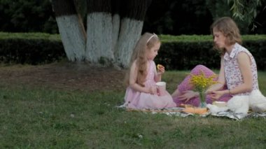 Mutlu anne ve kızı peçe üzerinde çay içiyor. Sıcak bir akşam günbatımında pikniğe üzerinde bir şehir parkı ailesinde... 4k