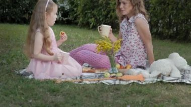Mutlu anne ve kızı peçe üzerinde çay içiyor. Aile içinde sıcak bir akşam günbatımında pikniğe üzerinde bir şehir parkı.