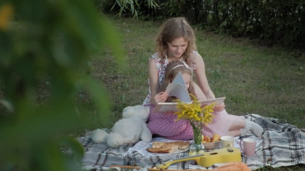 Mutlu anne ve kızı bir kitap okumak bir albümdeki fotoğrafları. Aile içinde sıcak bir akşam günbatımında pikniğe üzerinde bir şehir parkı. — Stok video
