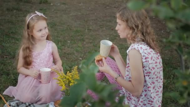 Eine glückliche Mutter und ihre Tochter trinken Tee auf dem Schleier. Familie im Stadtpark bei einem Picknick an einem warmen Abend bei Sonnenuntergang. — Stockvideo
